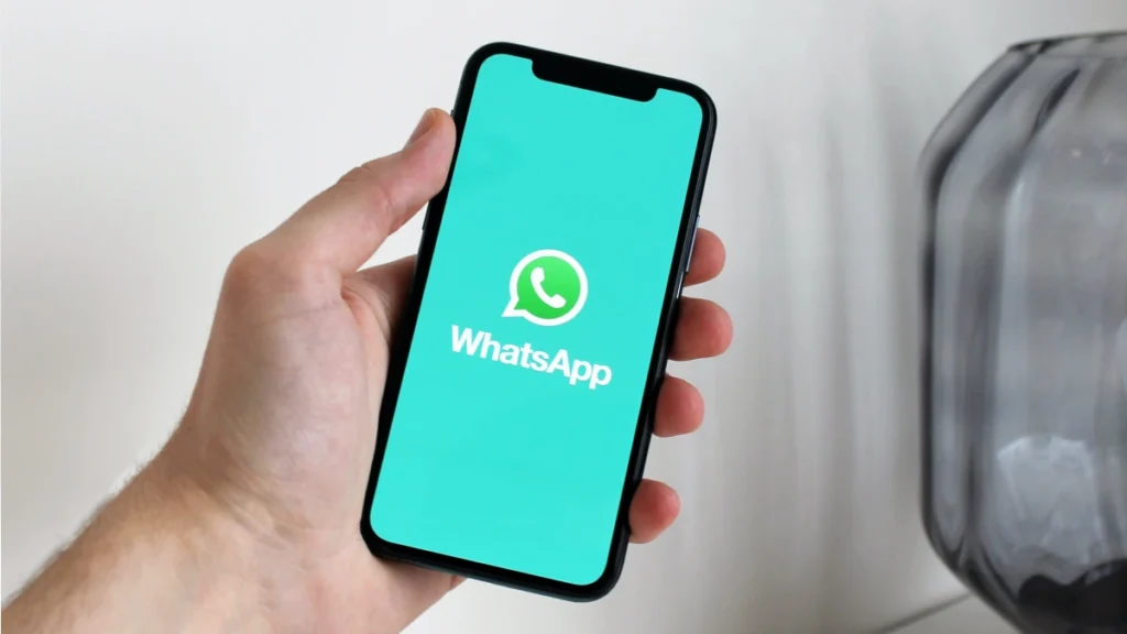 mão segurando smartphone. No smartphone, logotipo do WhatsApp